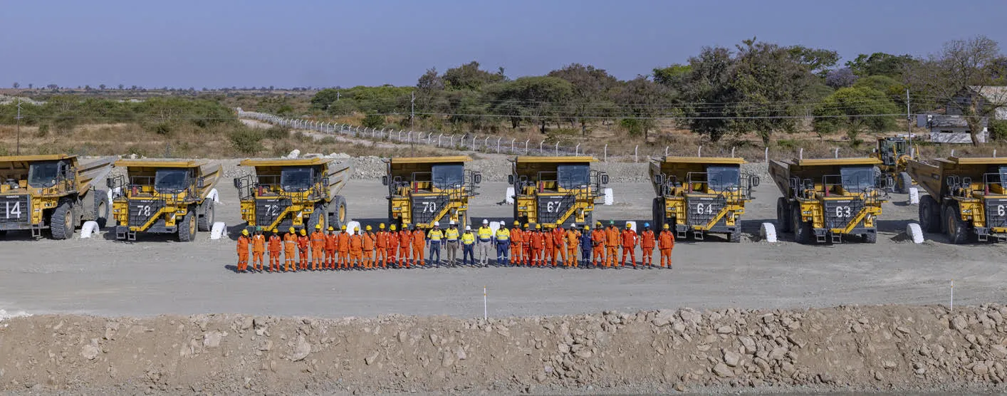 Taifa crew in orange coveralls in front of a line of haul trucks